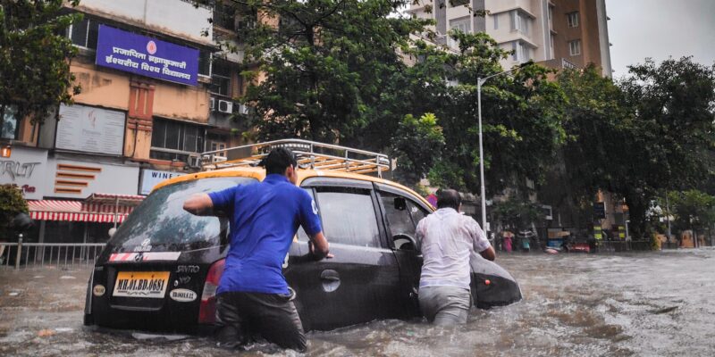 Two men push a car through a flooded street. The water is up to their hips.