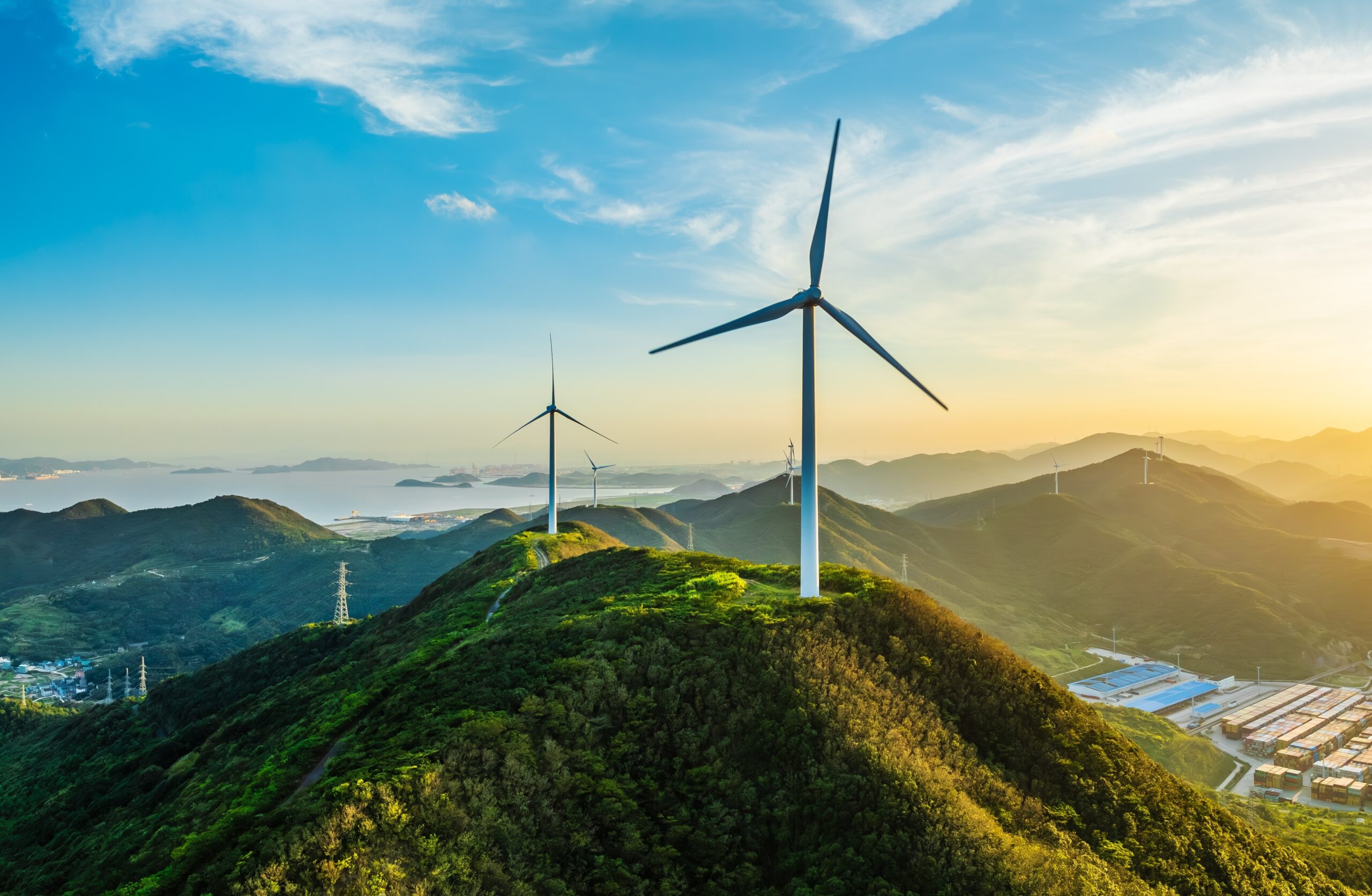 Photograph of wind turbines on the top of a mountain range agaunst a blue and yellow sky.